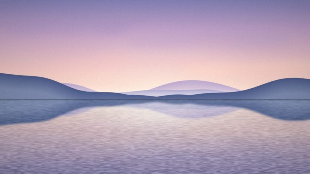 Calm misty lake at dawn reflecting a pale pink sky and layered blue hills