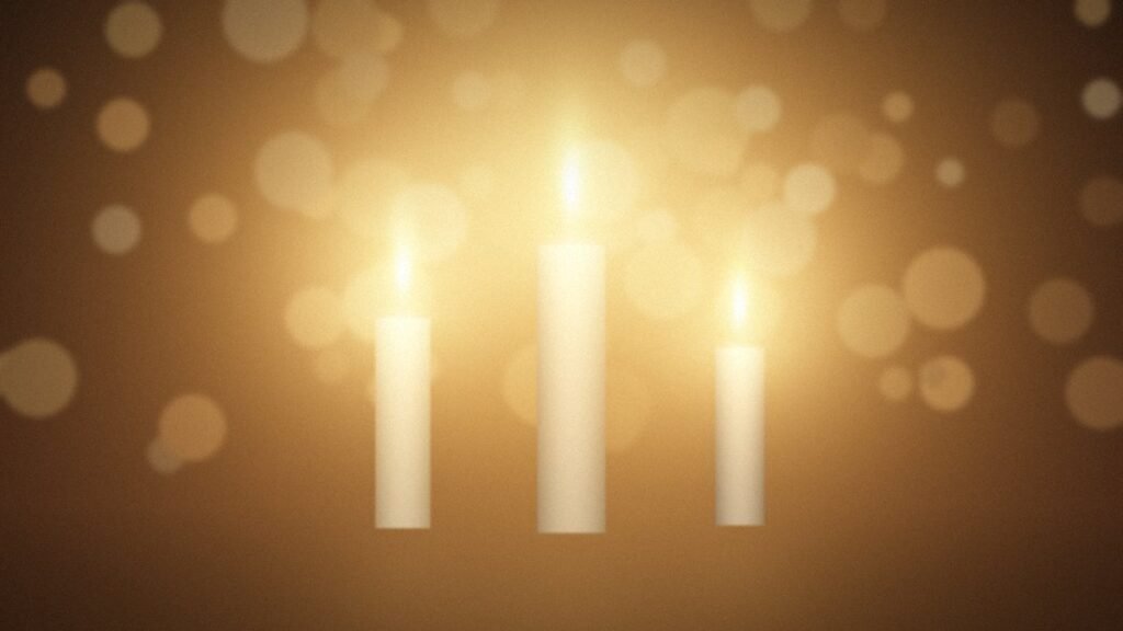 Warm candle flames glowing with golden bokeh lights in a dark room